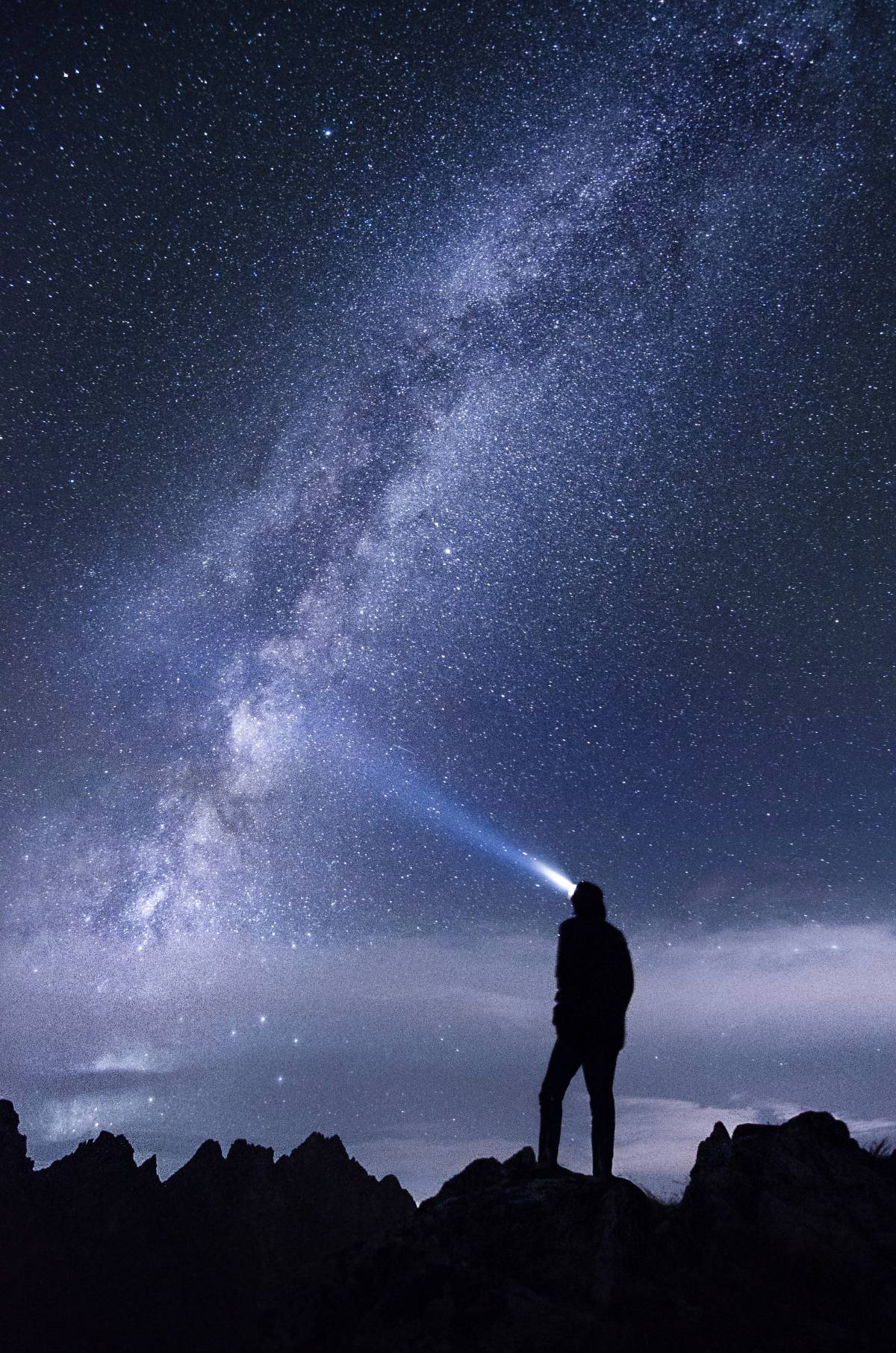 Mann steht mit Kopflampe im Dunkeln und schaut in den Himmel mit Sternen
